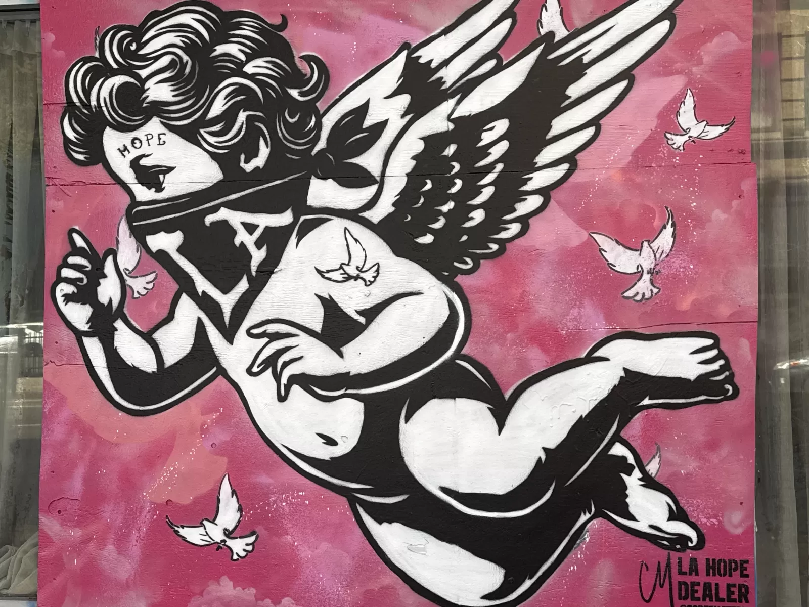 A black-and-white winged figure appears against a pink background, surrounded by white doves. The word “HOPE” is visible on the figure’s face, and partial text reading “LA HOPE DEALER” appears near the lower right.