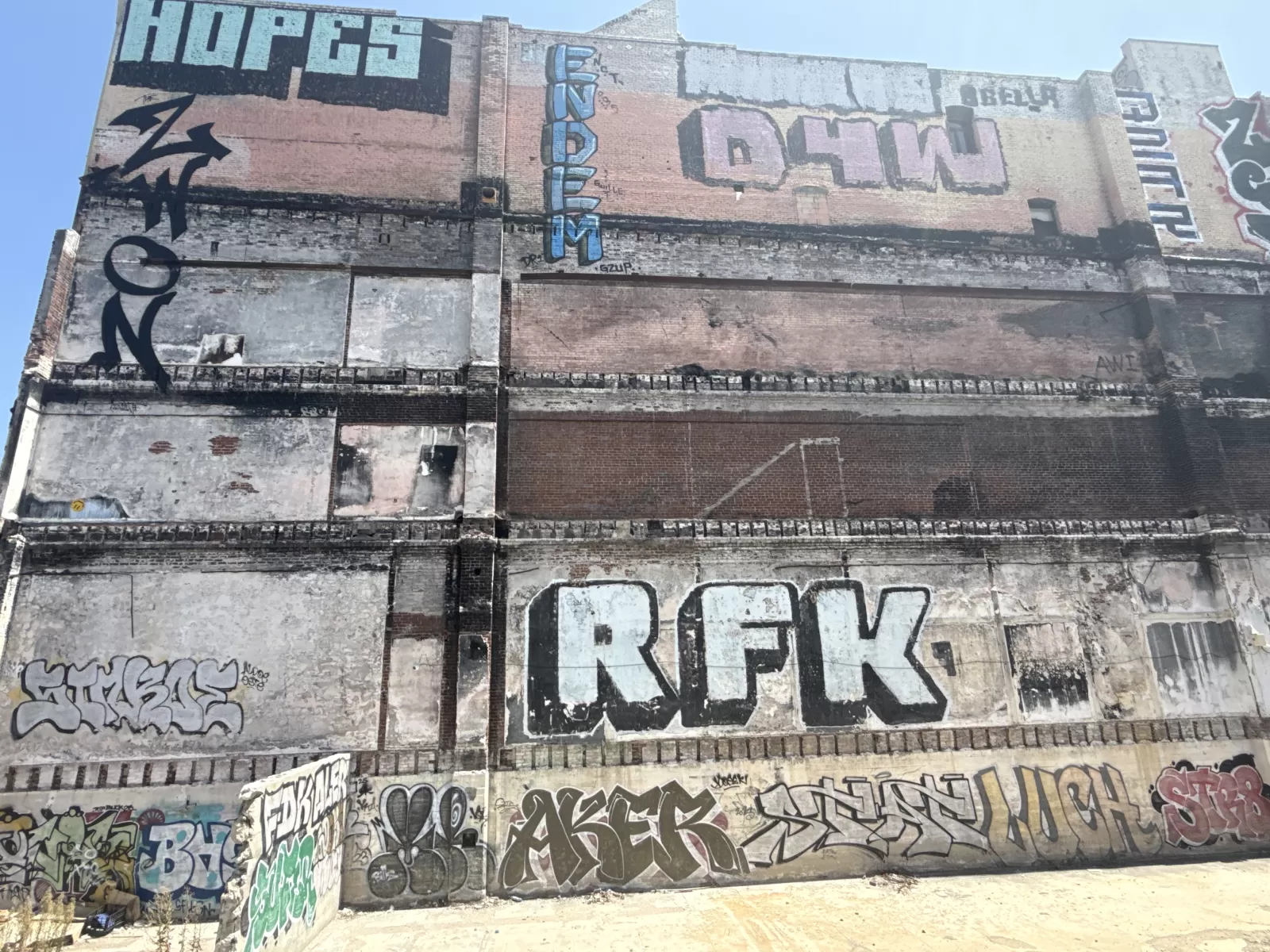 A large, weathered brick building is covered with overlapping graffiti-style lettering and tags in black, blue, white, gray, green, and red. Visible lettering includes “HOPES” near the upper left, vertical blue letters near the center, and large block letters including “REK” across the middle-lower section.